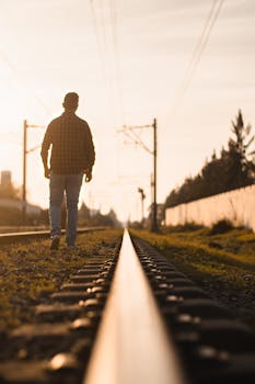 A lone figure walks along a railway track during sunrise, evoking a sense of journey and solitude.