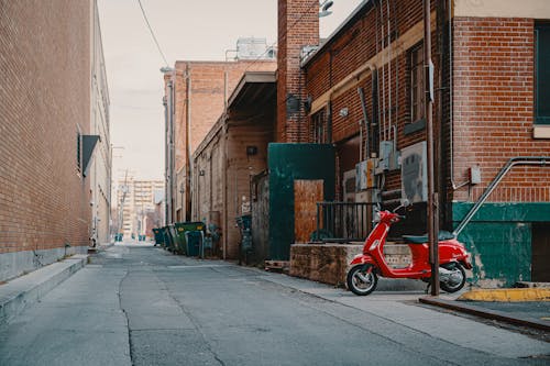 Aged house facades with shabby brick walls between empty asphalt roadway with cracks and parked moped under sky in town