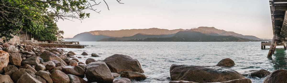 Calm seascape with rocks and mountains at sunset in Ilhabela, Brazil.
