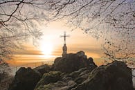 岩石山顶上立着十字架，周围树木环绕，构成迷人的日出景观