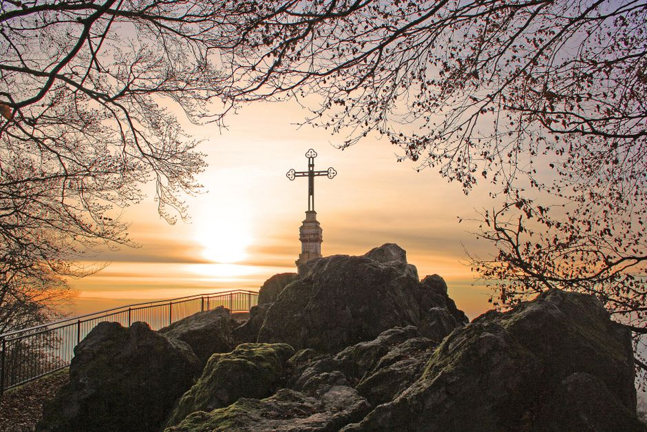 A cross atop a rocky summit surrounded by trees at sunrise