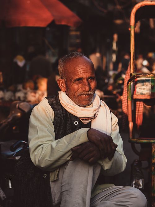 Free Pensive stylish senior ethnic male with gray hair and mustache sitting with crossed legs on street in town while looking away in daylight Stock Photo