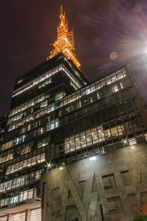 Low angle of modern style house with shining windows and decoration with letters on wall with golden tower on top under glowing street light in evening in town