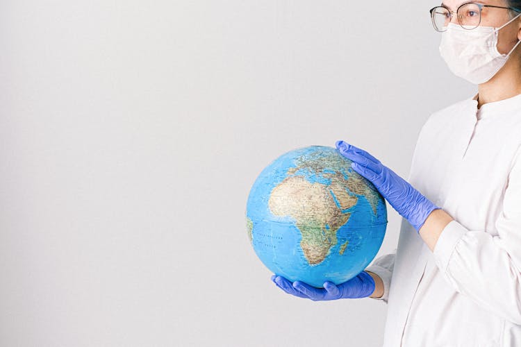 Person With A Face Mask And Latex Gloves Holding A Globe