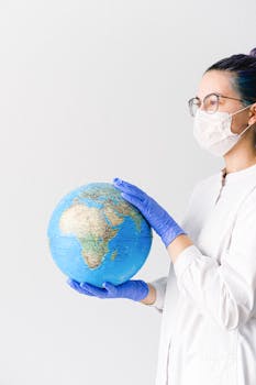 Healthcare worker wearing mask and gloves holds globe, symbolizing global pandemic response.