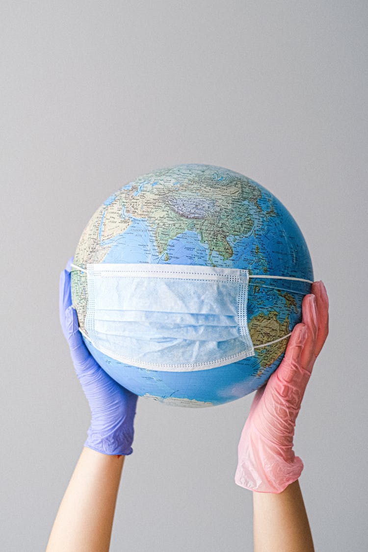 Hands With Latex Gloves Holding A Globe With A Face Mask