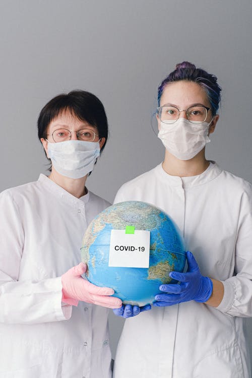 People With Face Masks and Latex Gloves Holding a Globe