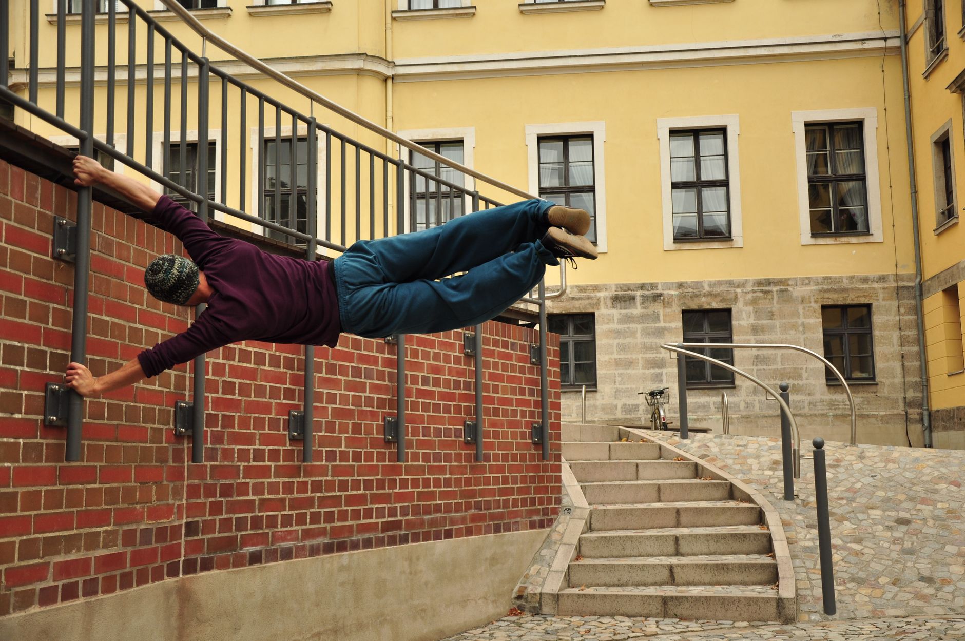A man performs parkour on a railing against a brick wall in an urban setting, showcasing agility and motion.