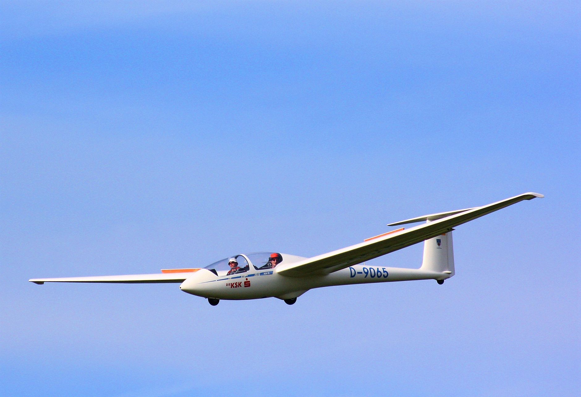 A two-seater glider flying gracefully against a backdrop of clear blue sky.