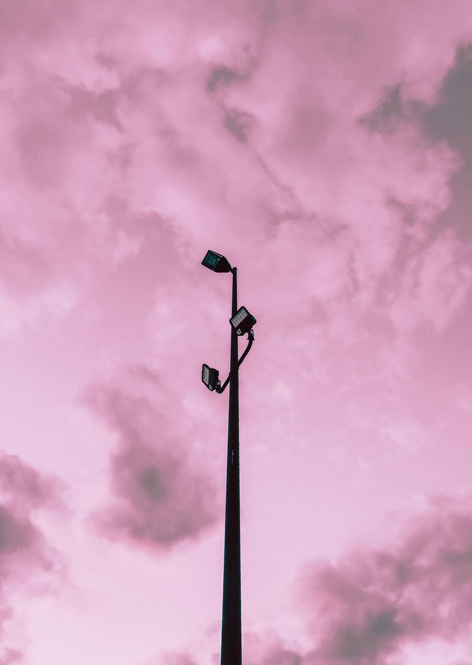 From below of high lamp post under colorful sky with clouds of different pink color shades in twilight at sunset in town