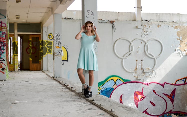 Stylish Woman In Headphones Standing Near Old Shabby Wall