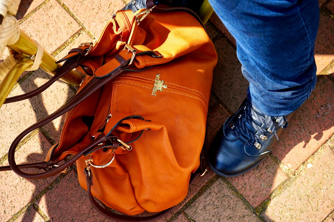 Free Person in Blue Denim Jeans and Black Leather Shoes Standing Beside Orange Leather Bag Stock Photo