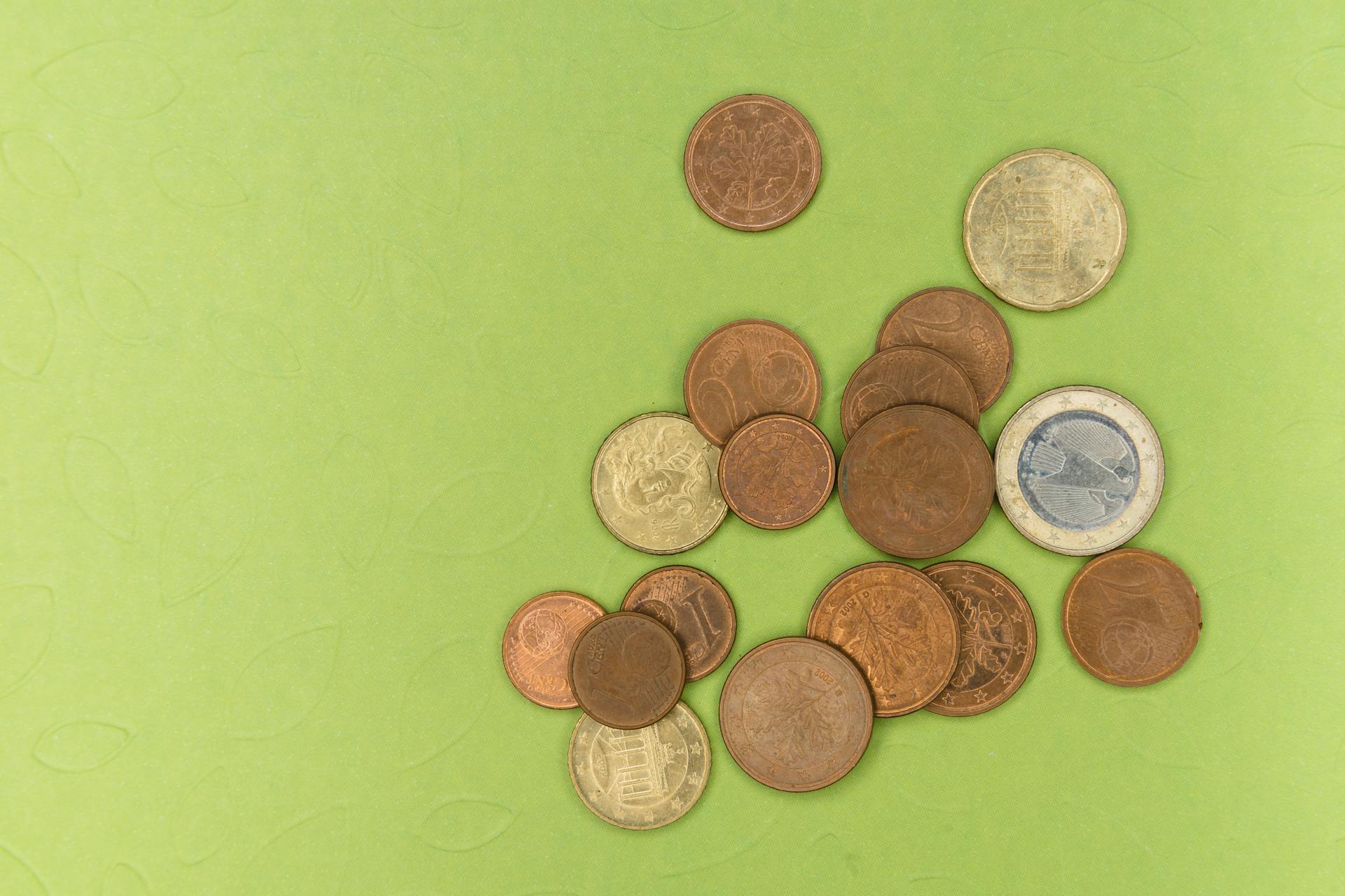 A collection of euro coins scattered on a green textured background, photographed in studio light.