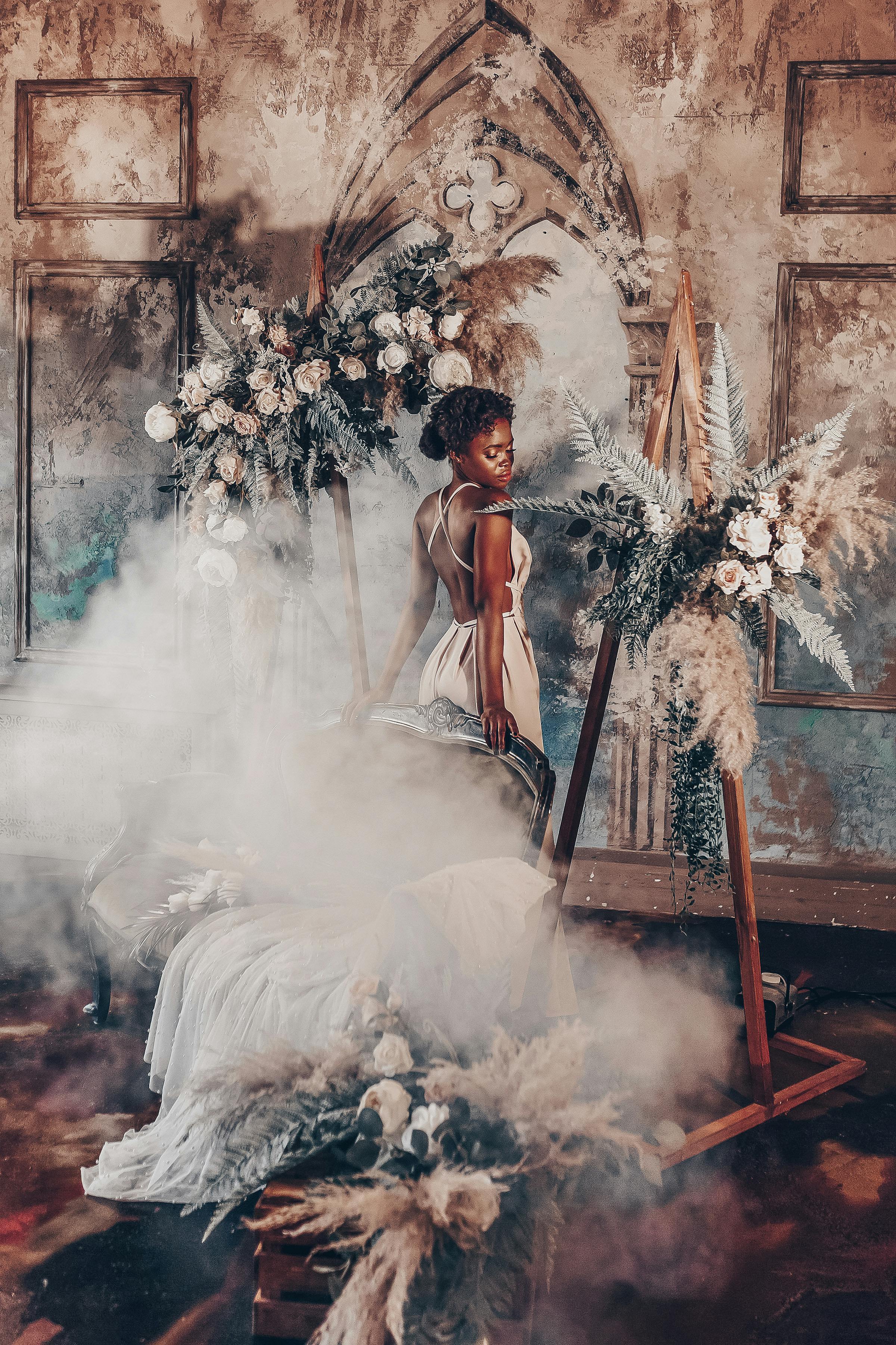 一名身穿优雅连衣裙的女子站在雾气缭绕的花卉主题室内场景中