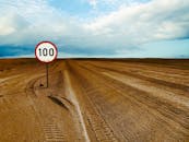 广阔的沙漠道路上，有明显的限速100标志，天空多云