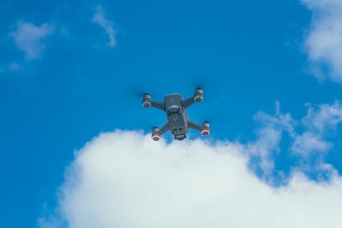 From below of modern unmanned aerial vehicle with propellers flying under bright sky with thick cloud in daylight