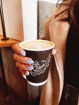 A hand with blue nails holds a hot latte in a cozy cafe setting, evoking warmth.