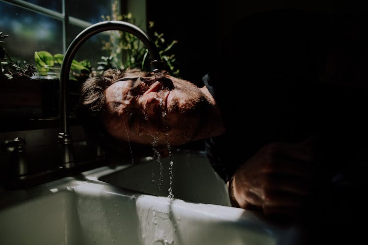 Man Washing Face In Kitchen Sink