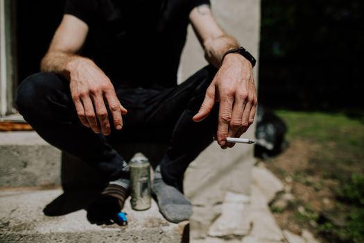 Unrecognizable male in socks sitting on steps with cigarette in hand and bottle of alcohol drink