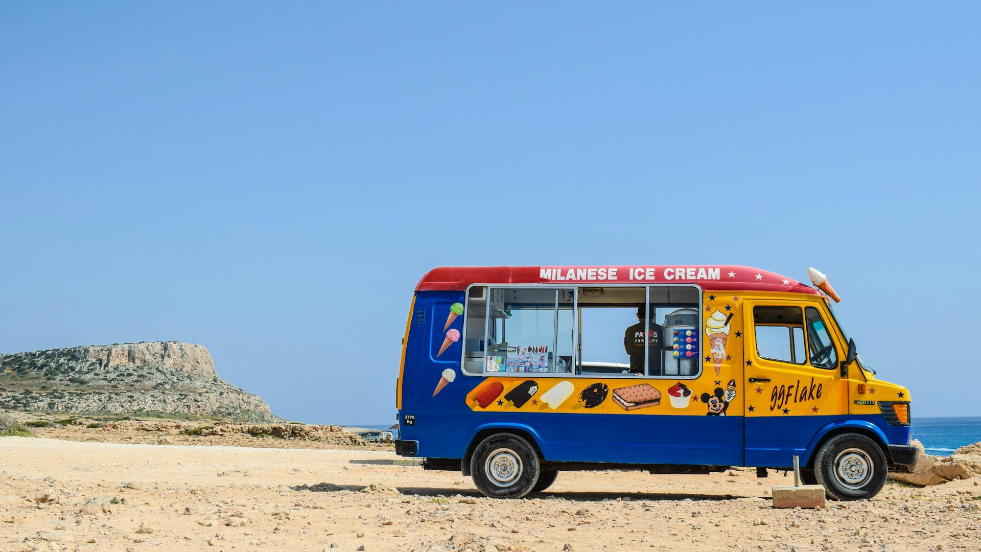 A vibrant ice cream truck parked on a sunny beach with clear blue skies.
