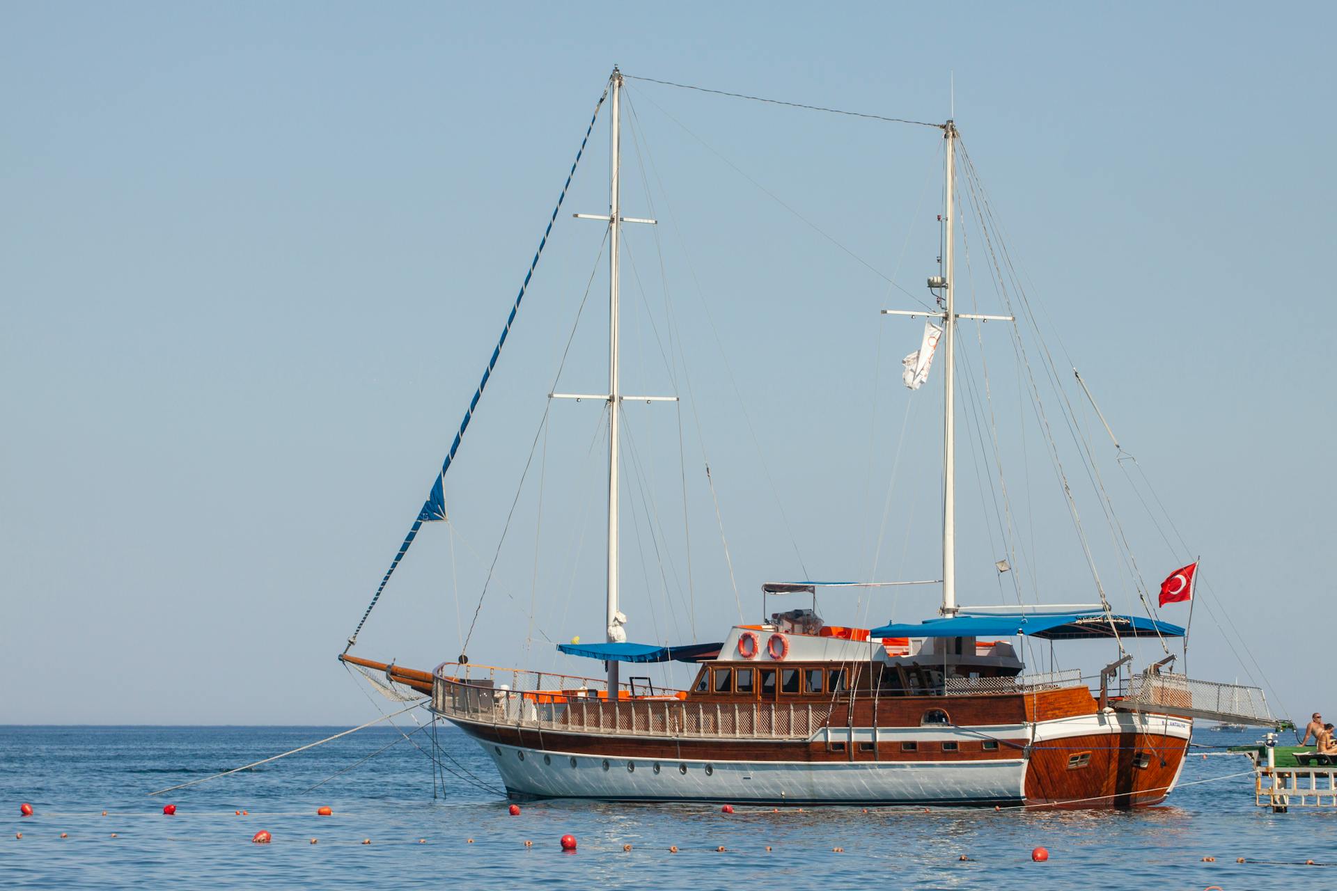 A beautiful wooden Turkish gulet sailboat anchored in calm Mediterranean waters under a clear blue sky.
