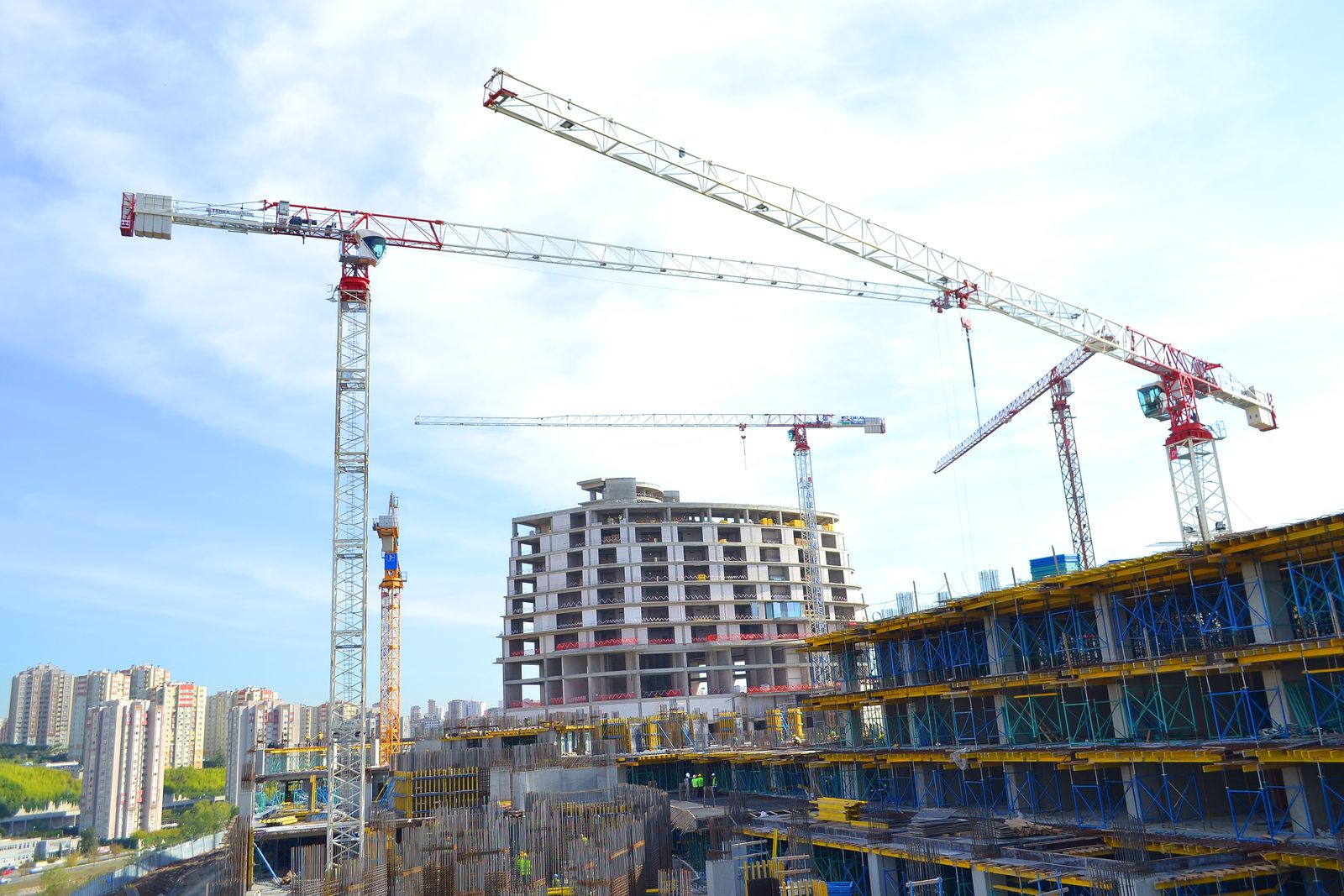 Multiple tower cranes over a mid-rise building under construction against a city skyline