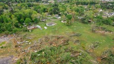 Drone view of uprooted trees heaped on green meadow in small village after massive storm