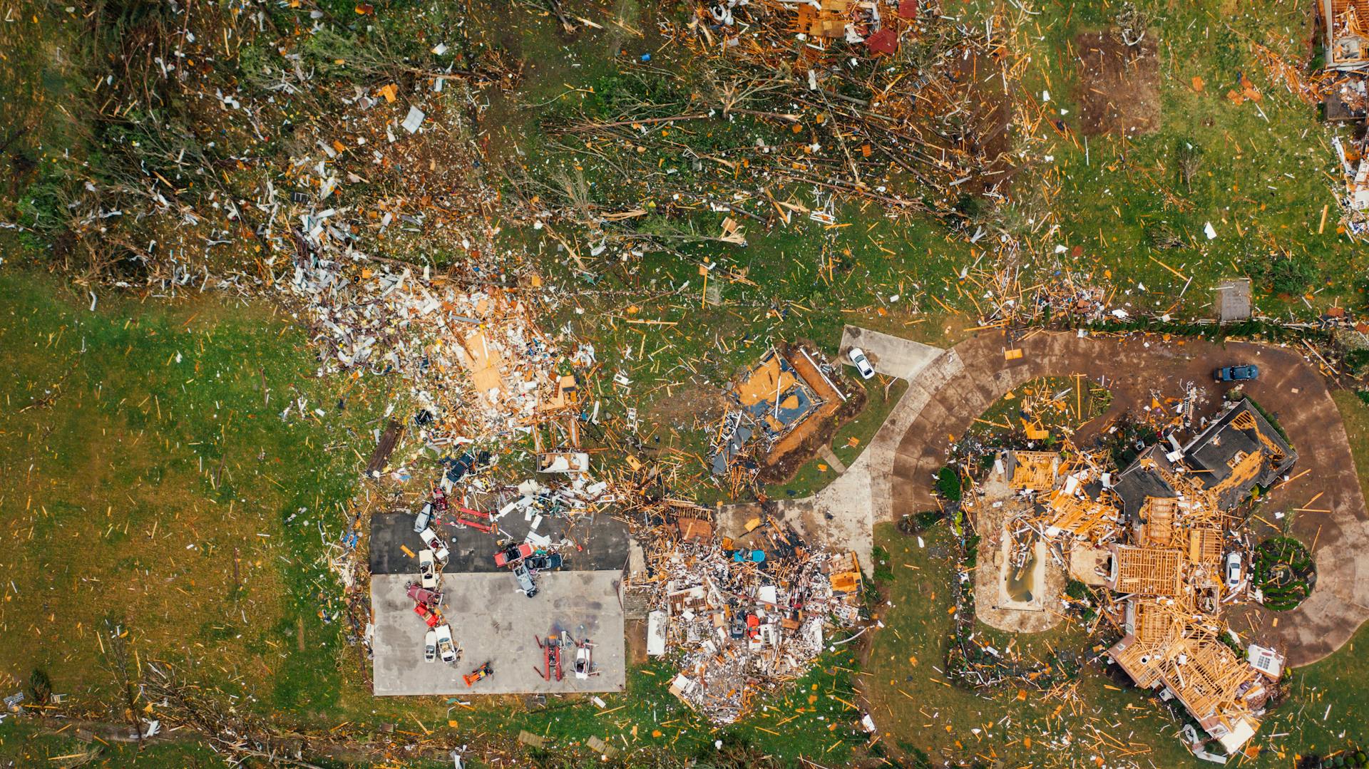 Aerial view of dramatic consequences of massive hurricane with ruined houses and kindling woods lying on green lawn