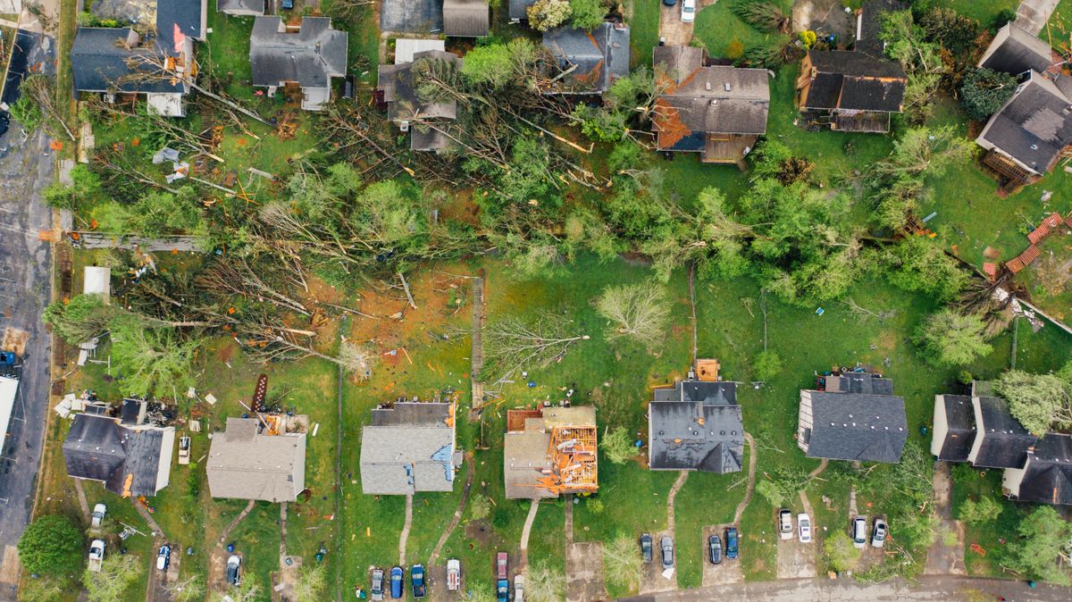 Drone view of storm-damaged homes with torn roofs and windthrown trees