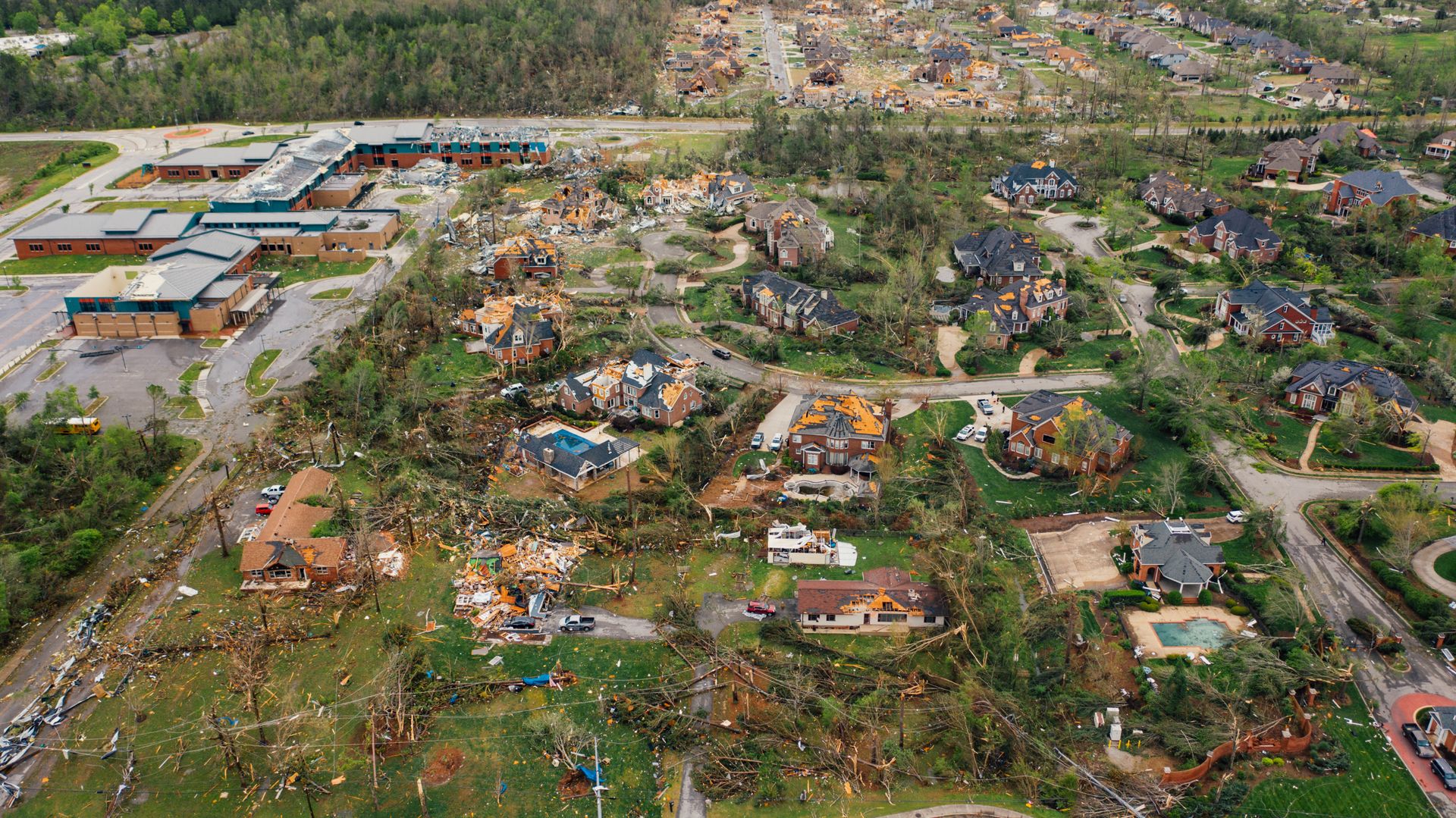 Aerial view of storm-damaged homes with downed trees and debris