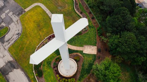 Free Drone view of big white cross statue located on green grassy terrain near lush trees in countryside Stock Photo
