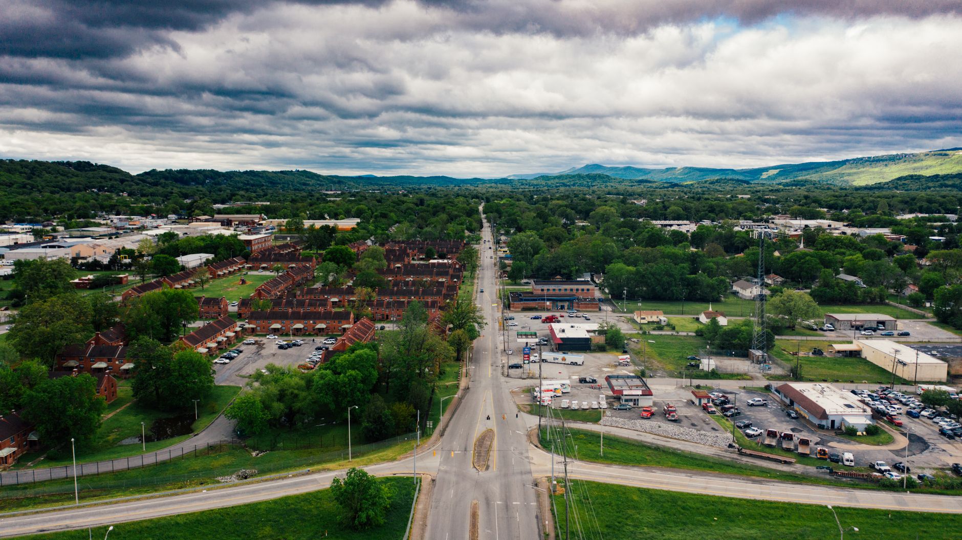 Aerial view of contemporary suburban settlement with narrow road and low level buildings amidst lush trees under scenic cloudy sky