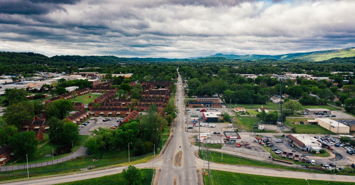 Aerial view of contemporary suburban settlement with narrow road and low level buildings amidst lush trees under scenic cloudy sky