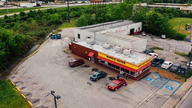 Drone view of contemporary small street cafeteria located near busy road in suburb district