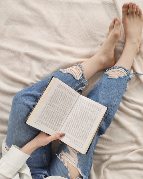 Free Crop unrecognizable woman reading book on comfy bed Stock Photo