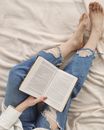 Crop unrecognizable woman reading book on comfy bed