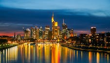 法兰克福的明亮天际线在夜间倒映在河中，展现出标志性建筑和充满活力的城市灯光