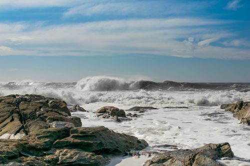Free Dramatic ocean scene with powerful waves crashing against a rugged rocky shore under a clear blue sky. Stock Photo
