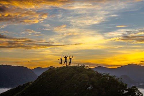 Free People with Raised Arms on Top of the Mountain at Sunset  Stock Photo