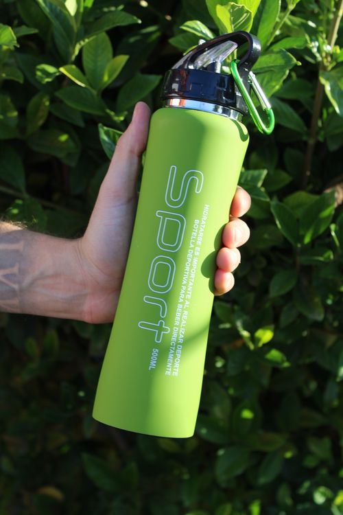 Free A close-up of a hand holding a green sports water bottle outdoors with greenery in the background. Stock Photo