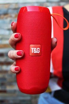 Vibrant red portable speaker held by a hand with matching red nails, showcasing a stylish tech accessory.