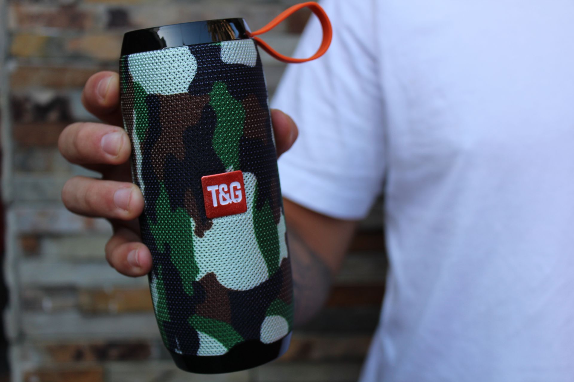 A close-up view of a camouflage-designed portable speaker being held by a person.