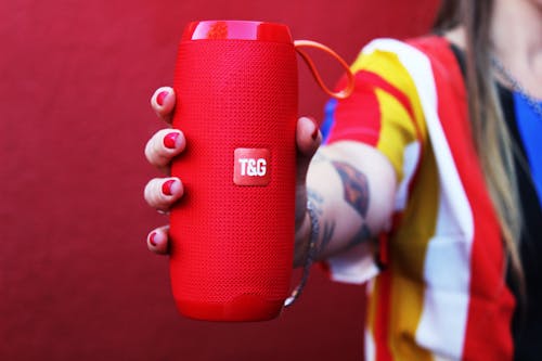 Unrecognizable woman demonstrating portable speaker against red background