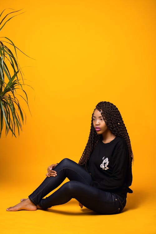 Trendy young black lady sitting in yellow studio
