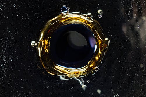 Closeup of droplet hitting surface of dark liquid and creating round shaped swirl and splashes as background