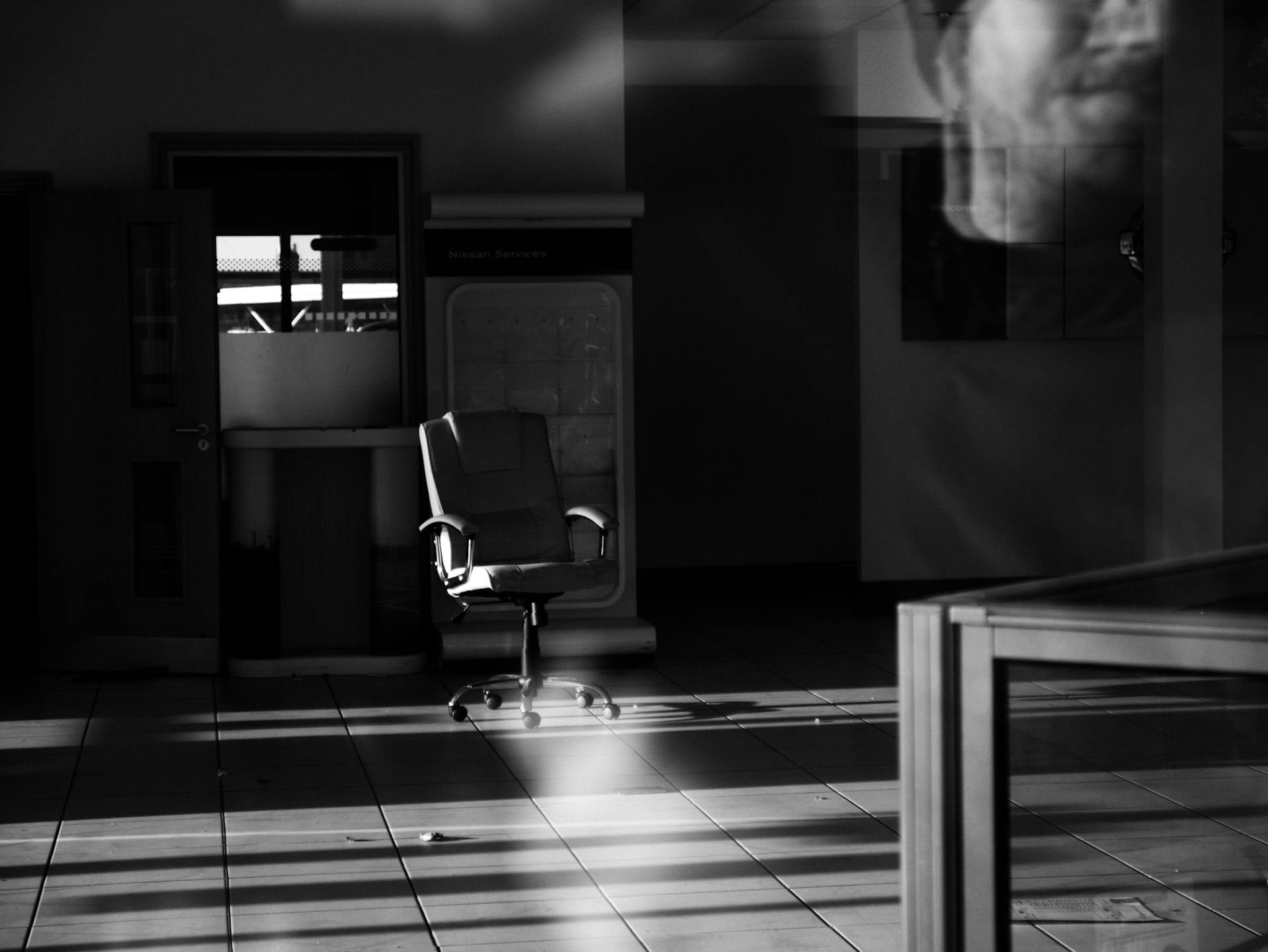 A black-and-white photo of an empty office space with a single chair and dramatic lighting.