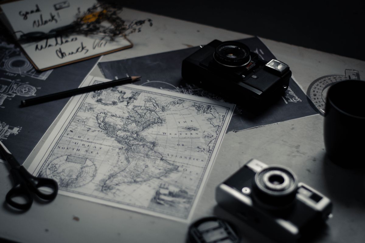Electronic devices for taking photo and scissors with pencil composing with herbarium and detailed map of world on table in room