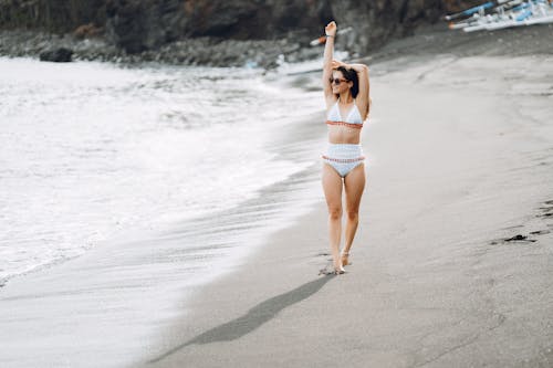 Joyful woman in swimsuit walking along seashore