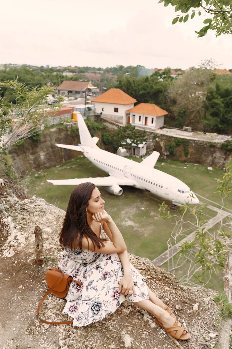 Positive Woman Sitting On Ground Against Private Jet