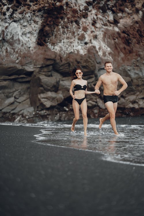Happy couple running on sandy beach with waving water